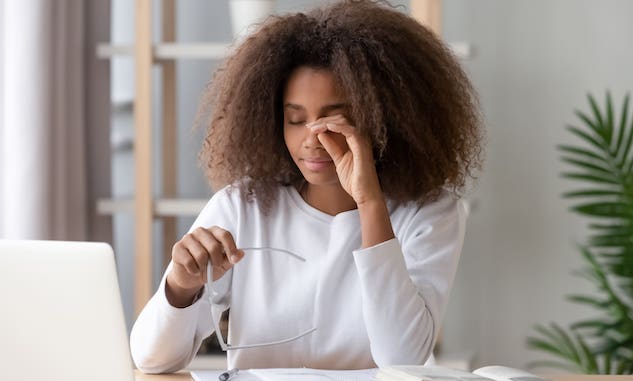 Woman sitting in front of a laptop, rubbing her eyes