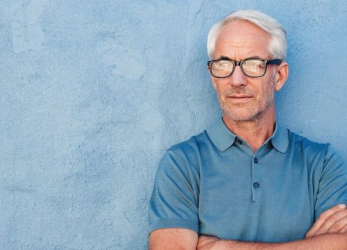 Older man with glaucoma posing in front of a blue wall