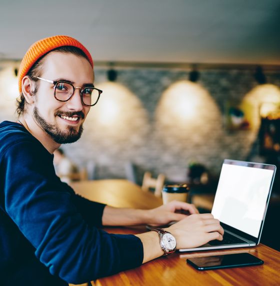 Man wearing a beanie and glasses using a laptop at a cafe